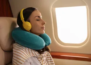 femme se relaxant avec un oreiller pour le cou et des écouteurs dans un avion